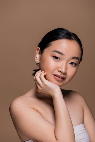 Portrait of smiling asian model looking at camera isolated on brown  - Fotografie, Obrázek
