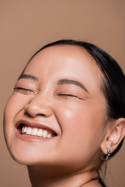 Portrait of pleased asian model closing eyes isolated on brown  - Φωτογραφία, εικόνα