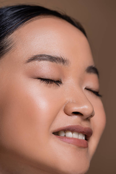 Close up view of smiling asian model with natural makeup isolated on brown  - Foto, afbeelding