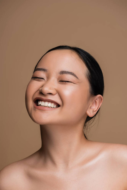 Cheerful asian woman with visage and naked shoulders standing isolated on brown  - Photo, Image