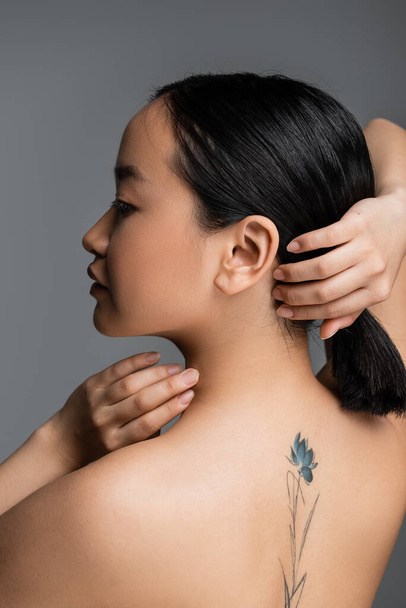 Side view of tattooed asian woman touching hair isolated on grey  - Valokuva, kuva