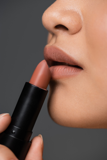Close up view of woman applying beige lipstick isolated on grey  - Photo, image