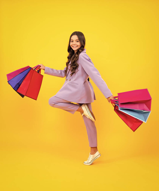 Funny teen girl hold shopping bag enjoying sale isolated on yellow. Run and jump. Portrait of teenager schoolgirl is ready to go shopping - Foto, Bild