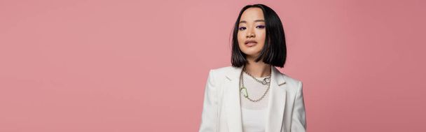 stylish asian woman in white jacket looking at camera isolated on pink, banner - Foto, afbeelding