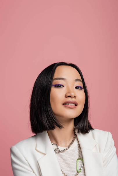 portrait of brunette asian woman in makeup and white jacket looking at camera isolated on pink - Valokuva, kuva