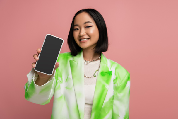 брюнетка азіатська жінка в модному зеленому і білому блістері, що показує смартфон з порожнім екраном ізольовано на рожевому
 - Фото, зображення
