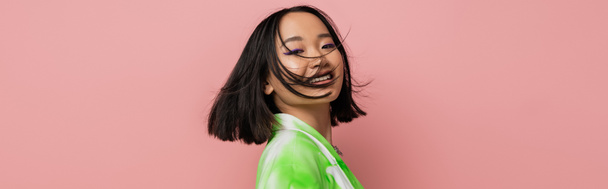 portrait of brunette asian woman with makeup smiling while posing isolated on pink, banner - Fotoğraf, Görsel