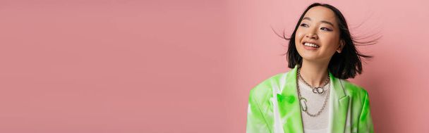 brunette asian woman in green and white blazer smiling and looking away isolated on pink, banner - Valokuva, kuva