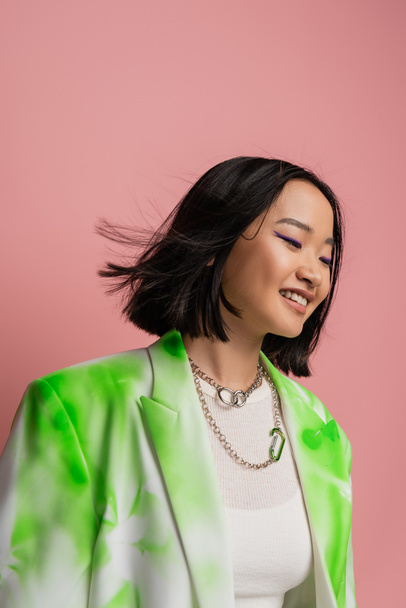 smiling asian woman in silver necklaces and fashionable jacket posing isolated on pink - Fotografie, Obrázek