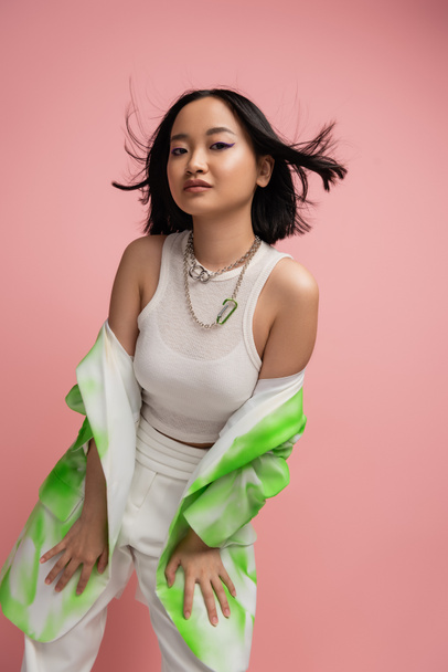 trendy asian woman in tank top and green and white blazer posing on wind isolated on pink - Φωτογραφία, εικόνα