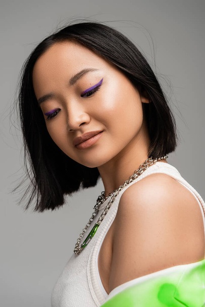 muotokuva brunette aasialainen nainen meikki ja violetti eyeliner eristetty harmaa - Valokuva, kuva