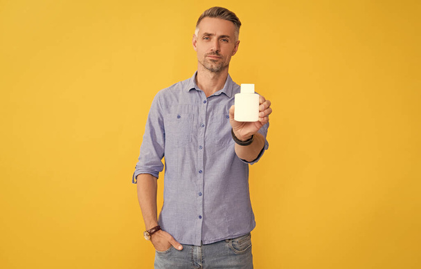 man hold pill jar on yellow background, health. - Foto, afbeelding