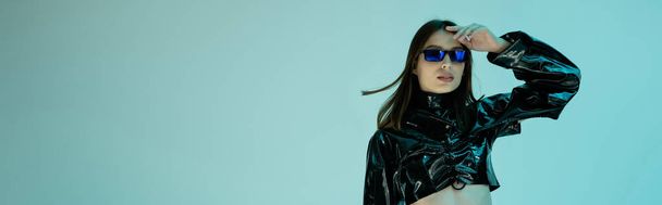 stylish young woman in black latex clothing and sunglasses standing isolated on blue, banner  - Foto, Bild