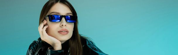 молода жінка в чорному латексному одязі і сонцезахисних окулярах ізольована на синьому, банер
  - Фото, зображення