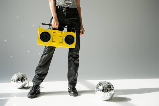 cropped view of woman in black leather pants holding boombox near disco balls on grey  - Foto, immagini