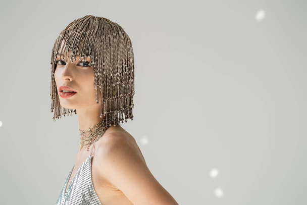 Trendy young woman in jewelry headwear looking at camera on grey background with light  - 写真・画像