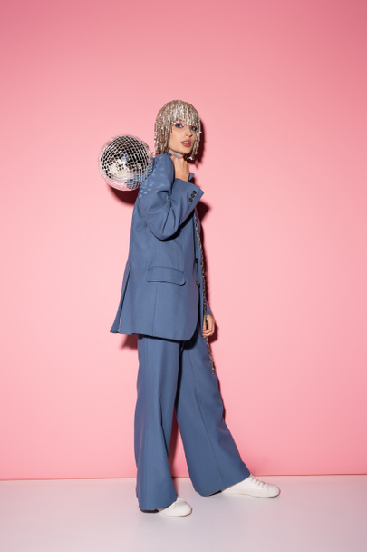 Full length of woman in blue suit and jewelry headwear posing with disco ball on pink  - Photo, Image