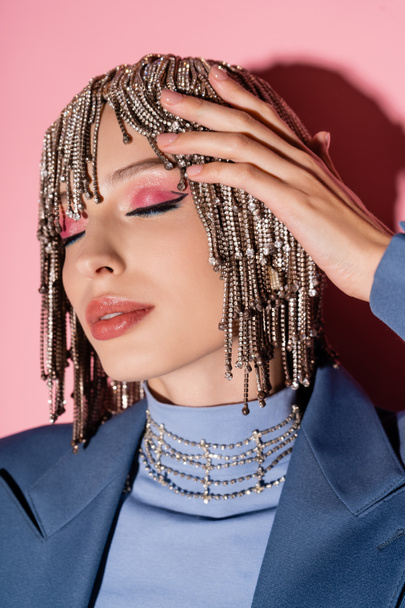 Portrait of trendy woman with makeup touching jewelry headwear on pink background  - Foto, Bild