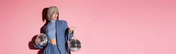 Trendy woman in luxury headwear and suit holding mirror balls on pink background, banner  - Foto, Bild