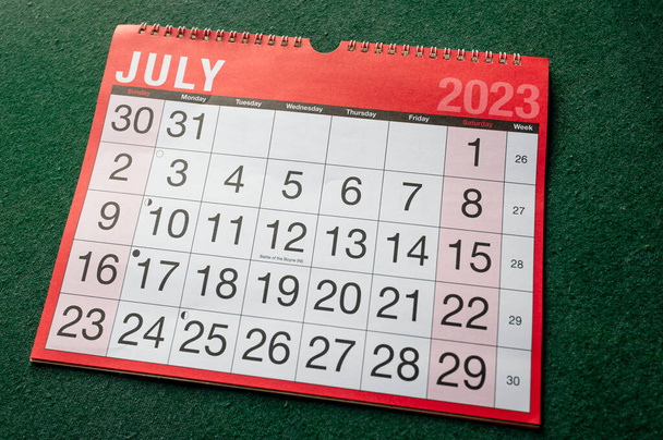 Calendario 2023, julio, planificador mensual. Organizador de día, mes, año, fecha y actividad, pared y escritorio. Calendario rojo y blanco con letras y números grandes sobre fondo verde. Se muestra en ángulo. - Foto, imagen