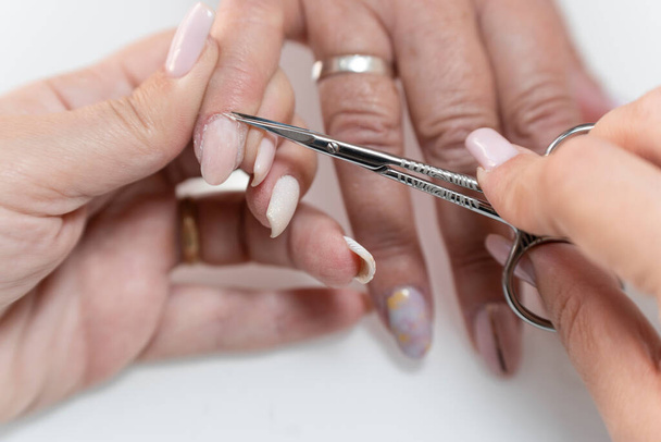 Close-up van een echte vrouwelijke manicure snijden van de nagel van een senior vrouwen vingernagel met een schaar - Foto, afbeelding