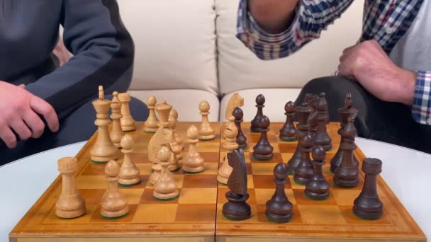 Zbliżenie dwóch męskich rąk grających w szachy, wykonujących ruchy na szachownicy z czarnym białym drewnianym kawałkiem w środku. Przyjaciele rozważają ruchy w logicznej grze planszowej. Rozrywka domowa, hobby - Materiał filmowy, wideo