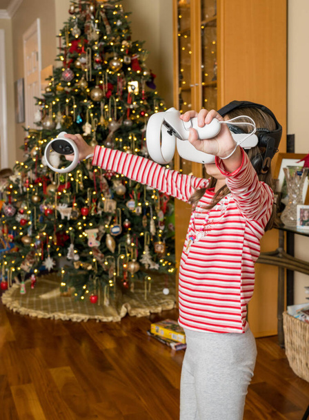 Junges Mädchen spielt zu Weihnachten ein Spiel auf einem modernen Virtual-Reality-VR-Headset - Foto, Bild