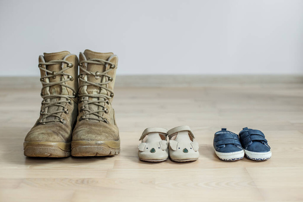 oude militaire laarzen en babyschoenen op houten vloer. Concept van militaire vader en familie. Kopieerruimte - Foto, afbeelding