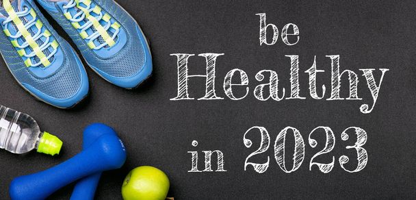 New year 2023 resolutions healthy lifestyle and sport. Be healthy in 2023. Motivation sport goals 2023 with sport equipment shoes, dumbbells, fruit and water bottle on black background - Photo, Image