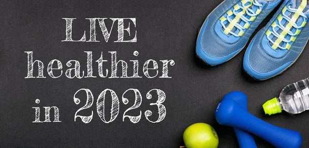 New year 2023 resolutions healthy lifestyle and sport. Be healthy in 2023. Motivation sport goals 2023 with sport equipment shoes, dumbbells, fruit and water bottle on black background - Photo, Image