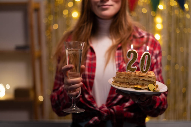 Hände einer jungen Frau mit Geburtstagstorte mit Kerzen Nummer 20 und einem Glas Champagner zum Geburtstag. Kopierraum - Foto, Bild