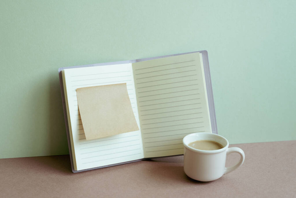 Abra el cuaderno y el bloc de notas pegajoso y la taza de café en el escritorio. fondo de pared de menta. espacio de trabajo, negocio, lugar de estudio - Foto, imagen