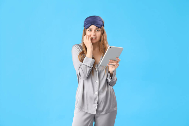 Mladá žena s tabletu počítač kousání nehty na modrém pozadí - Fotografie, Obrázek