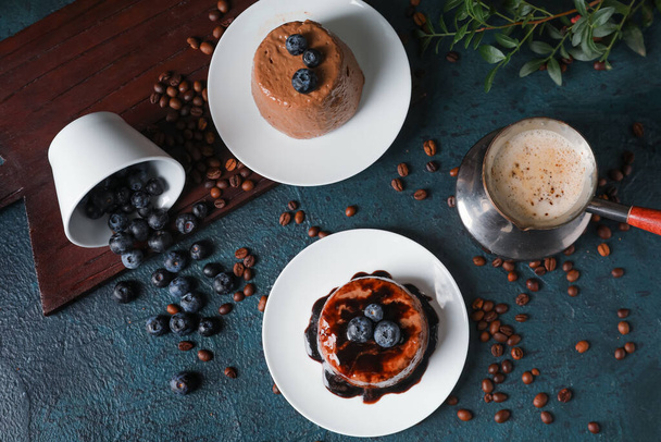 Πιάτα με νόστιμη πουτίγκα σοκολάτας, αναποδογυρισμένο φλιτζάνι βατόμουρο, κόκκους καφέ και καπουτσίνο σε jezve στο τραπέζι - Φωτογραφία, εικόνα