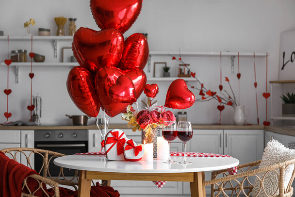 Τραπέζι φαγητού με δώρα, ποτήρια κρασί, κεριά, λουλούδια και μπαλόνια για την Ημέρα του Αγίου Βαλεντίνου στην κουζίνα - Φωτογραφία, εικόνα