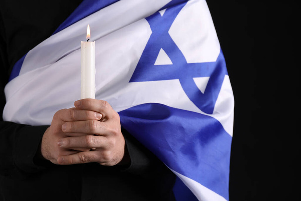 Jewish man with candle and flag of Israel honoring victims of Holocaust on dark background, closeup - Photo, Image