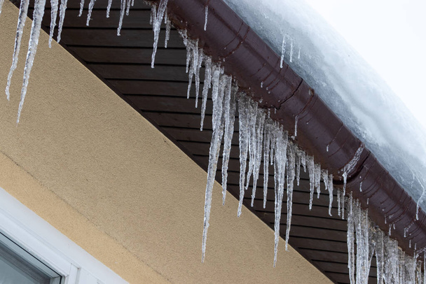 Isoja jääpuikkoja rivitalon katolla. Katto kodin peitetty jääpuikkoja talvella - Valokuva, kuva
