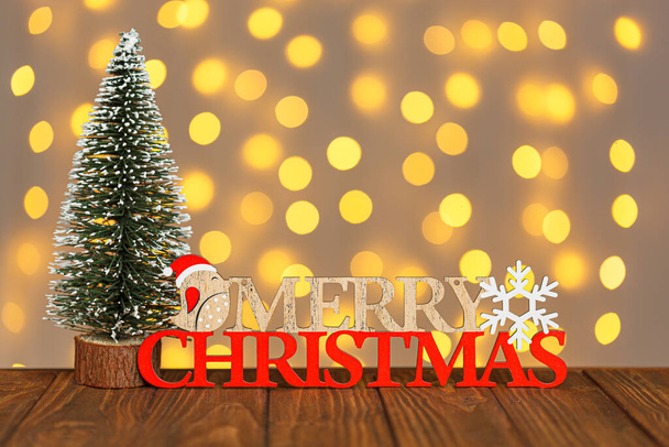 Árvore de Natal e a inscrição Feliz Natal contra o fundo de luzes embaçadas close-up - Foto, Imagem