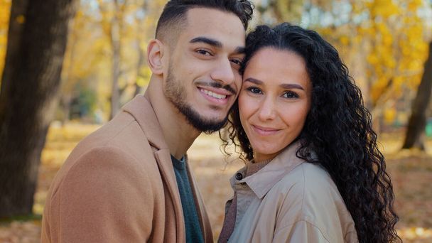 Close-up portret buiten Latijns-Amerikaanse etnische multiraciale paar verliefd in de herfst park op zoek naar camera man en meisje vrouw glimlachen staan dicht bij elkaar aanraken hoofden liefhebbers op romantische date - Foto, afbeelding