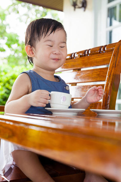 Pouco menina asiática sorrindo e segurando uma xícara de chá
 - Foto, Imagem