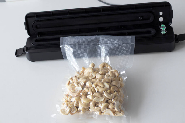 Süpürge ambalaj makinesi ve vakumlu fındık. Plastik bir kaju çantasıyla beyaz bir masaya yiyecek paketlemek için bir aygıt - Fotoğraf, Görsel