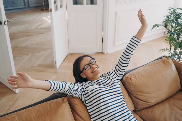 Top down of young serene woman stretching after daytime nap on sofa. Happy hispanic woman is having rest at home in weekend morning. Lady is relaxing on leather couch. Lazy day concept. - Photo, Image