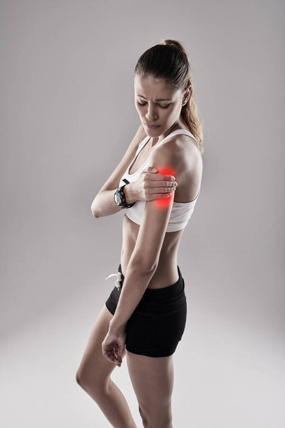 Belastungen können plötzlich auftreten oder sich im Laufe der Zeit entwickeln. eine junge Frau hält ihre verletzte Schulter, die rot hervorgehoben ist - Foto, Bild