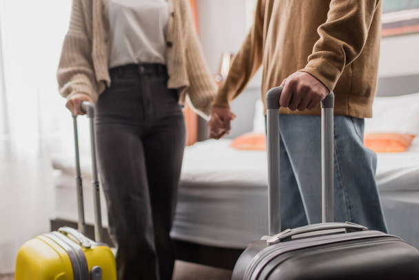 partial view of blurred couple with luggage holding hands in hotel apartments - Fotografie, Obrázek