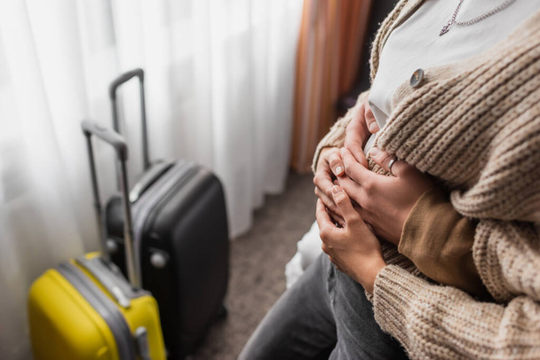 καλλιεργημένη άποψη του άνδρα αγκαλιάζει γυναίκα κοντά θολή ταξιδιωτικές τσάντες στα διαμερίσματα του ξενοδοχείου - Φωτογραφία, εικόνα