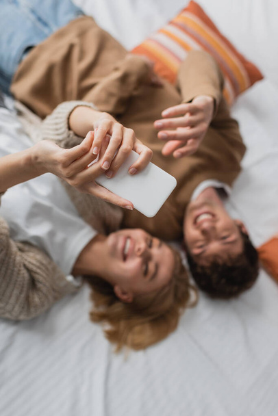 top view of blurred couple lying on bed in hotel and taking selfie on mobile phone - Photo, image