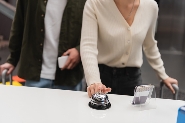 частичный вид женщины звонящей службы колокол на ресепшене рядом размытый парень со смартфоном в отеле - Фото, изображение