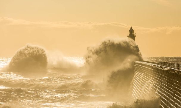 Nagy hullámok verik a Tyne torkolatát őrző világítótornyot és északi mólót Tynemouth-ban napkeltekor, Angliában. - Fotó, kép