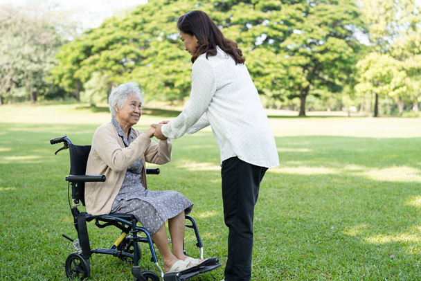 Pflegerin hilft und pflegt asiatische Seniorin oder ältere Dame Patientin im Rollstuhl im Park, gesundes starkes medizinisches Konzept. - Foto, Bild