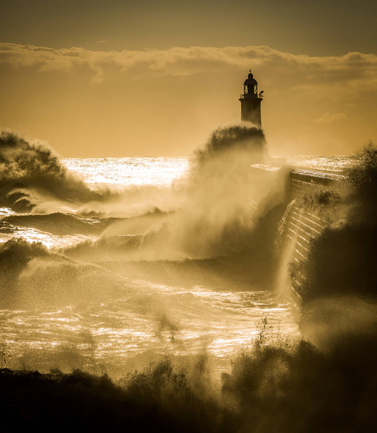 イギリス、日の出にタイネマスのタインの口を守る灯台と北の桟橋を打つ大きな波 - 写真・画像